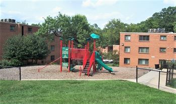 A playground with a red and green slide in front of a brick building.